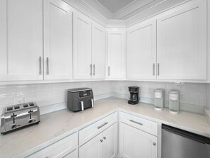A modern kitchen with white cabinetry, a toaster, a coffee maker, and two coffee dispensers. - The Fort - Gulf Coast Getaway (Gulf Shores)