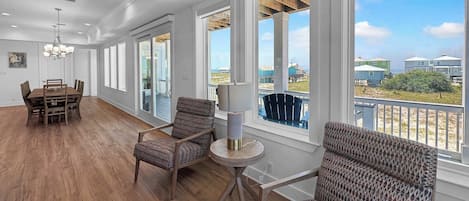 Amplia habitación con suelo de madera, una mesa de comedor, sillas y vistas a la playa a través de amplios ventanales.