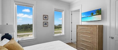 Un dormitorio con cama, cómoda, ventilador de techo y dos ventanas con vistas al exterior.