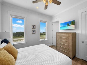 A bedroom with a bed, a dresser, a ceiling fan, and two windows with a view of the outdoors. - The Fort - Gulf Coast Getaway (Gulf Shores)
