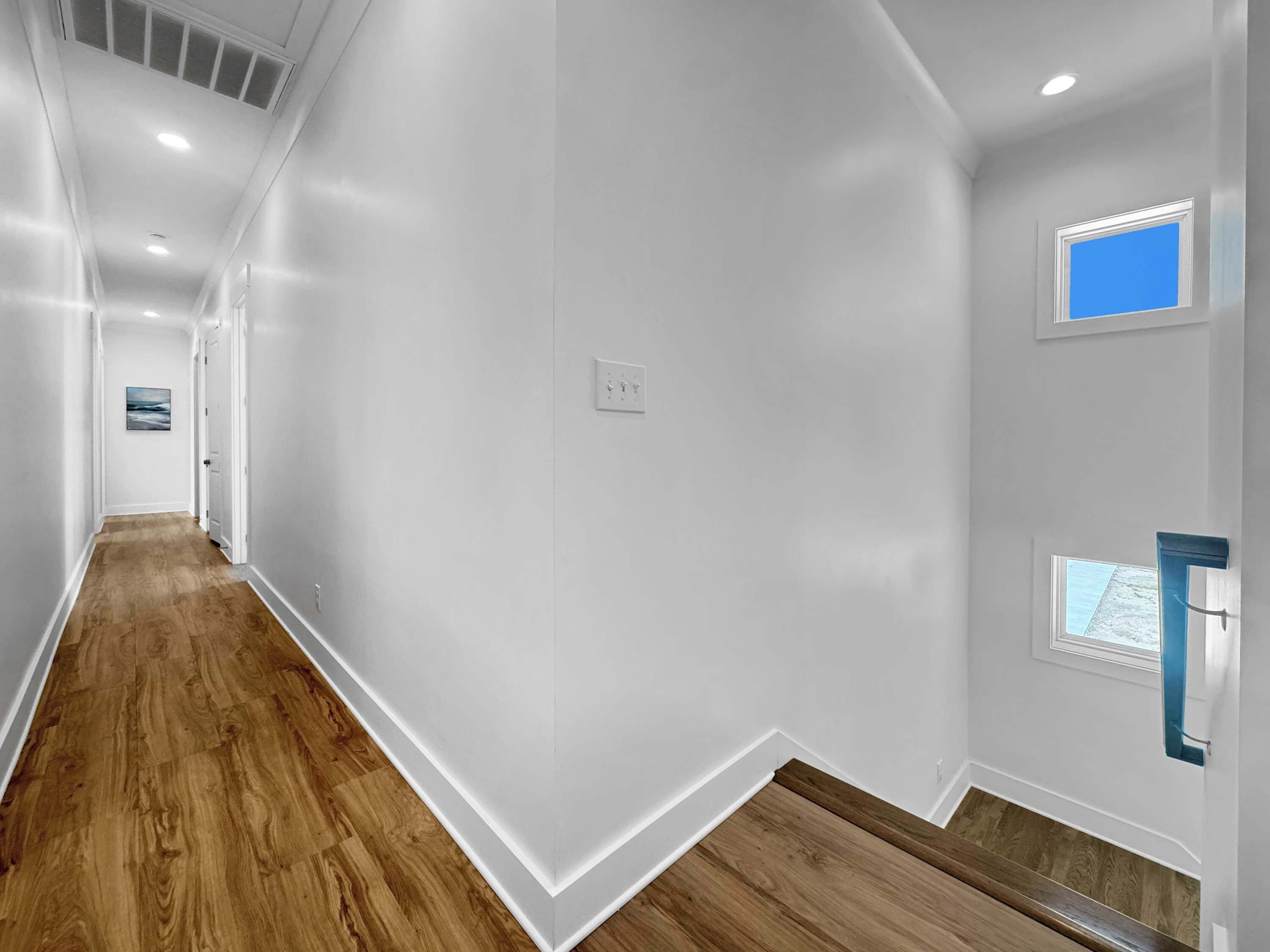 Un pasillo con suelo de madera, paredes blancas e iluminación empotrada.