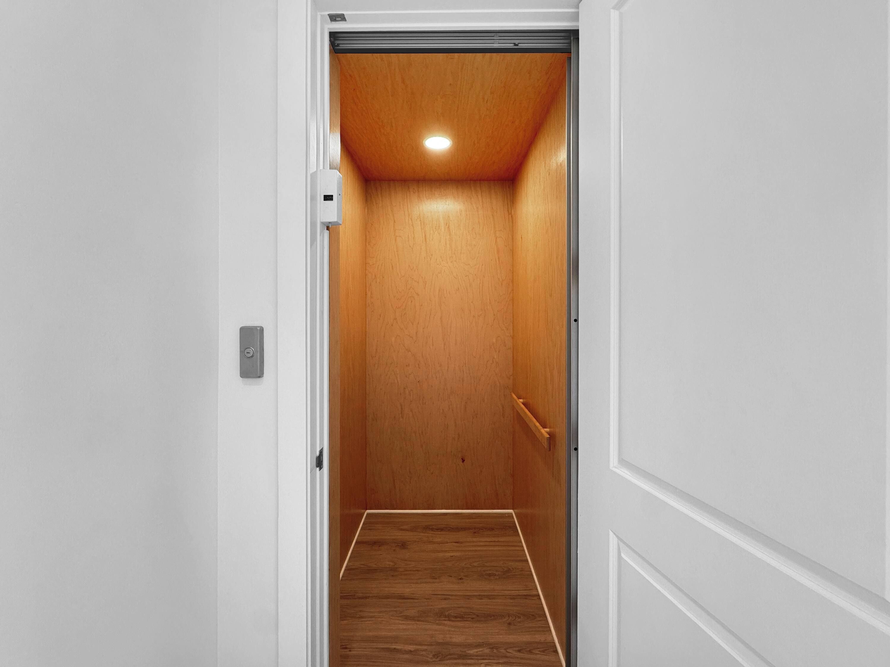 A narrow, wooden-paneled elevator shaft with a light fixture at the top and a handrail on the right side.