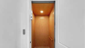 A narrow, wooden-paneled elevator shaft with a light fixture at the top and a handrail on the right side.