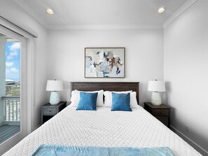 A hotel room with a large bed, two bedside tables, a painting on the wall, and a balcony with a view. - The Fort - Gulf Coast Getaway (Gulf Shores)