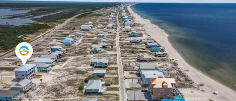 A coastal area with a row of beach houses along the shoreline, a road running parallel to the beach, and a body of water in the distance.