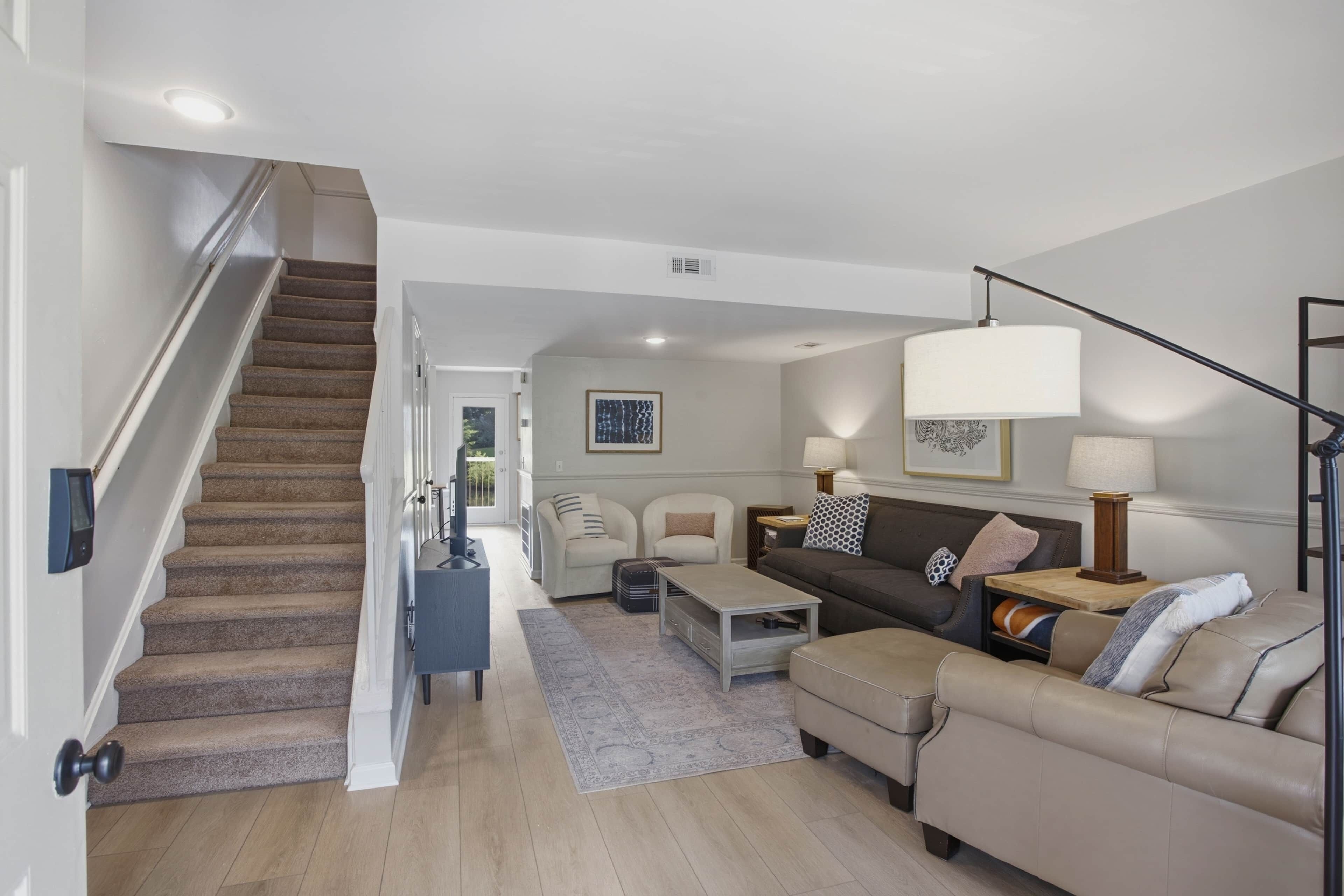 Una sala de estar moderna con una escalera, un conjunto de sofá, una mesa de centro y una lámpara.