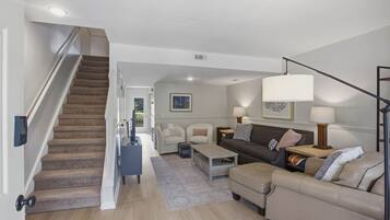 Una sala de estar moderna con una escalera, un conjunto de sofá, una mesa de centro y una lámpara.