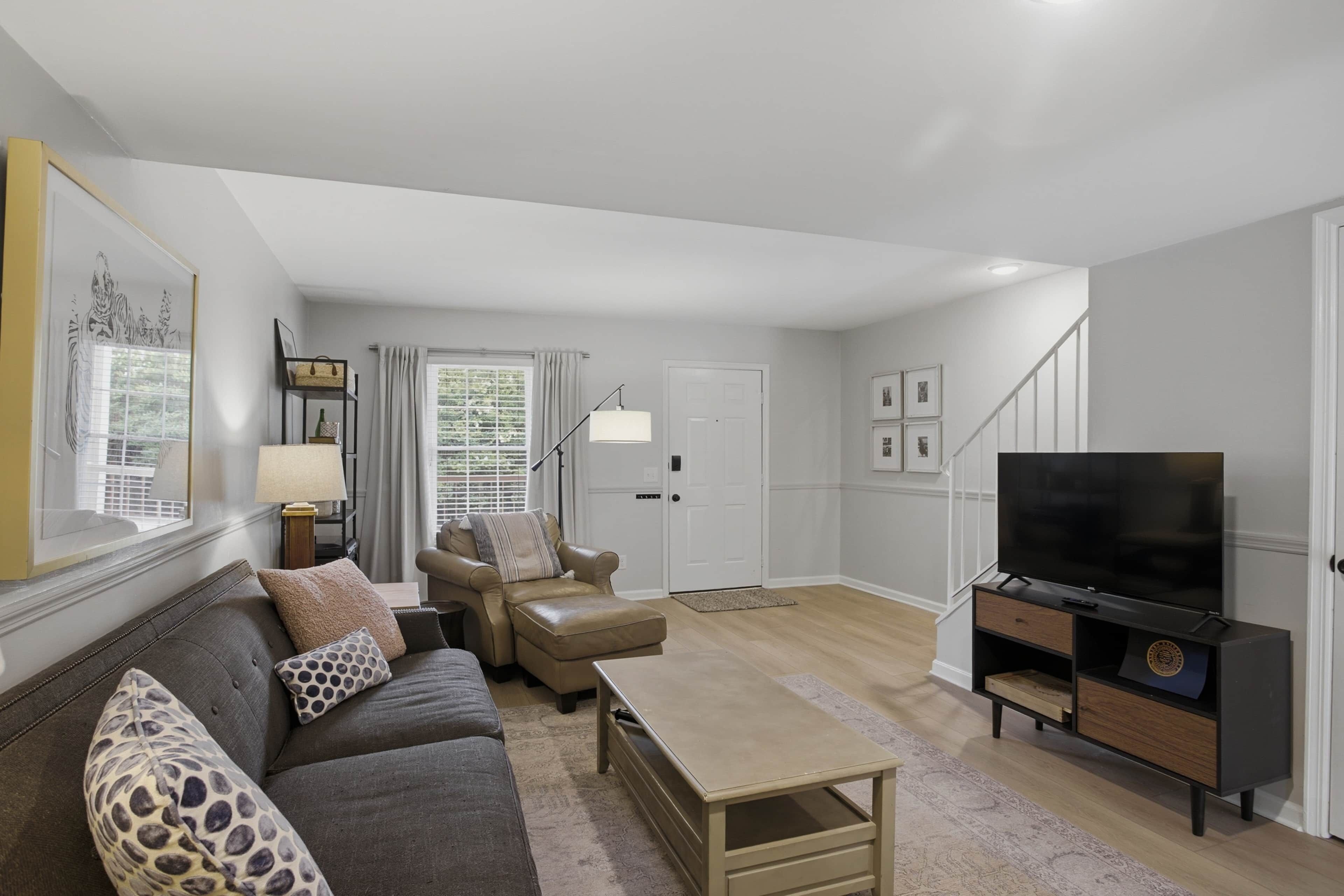 Ein Wohnzimmer mit Sofa, Sessel, Couchtisch, Fernseher und einer Treppe zu einer weiteren Ebene.