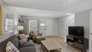 Ein Wohnzimmer mit Sofa, Sessel, Couchtisch, Fernseher und einer Treppe zu einer weiteren Ebene.
