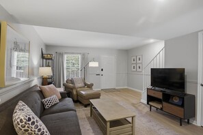 Een woonkamer met een bank, fauteuil, salontafel, televisie en een trap naar een hoger gelegen verdieping.
