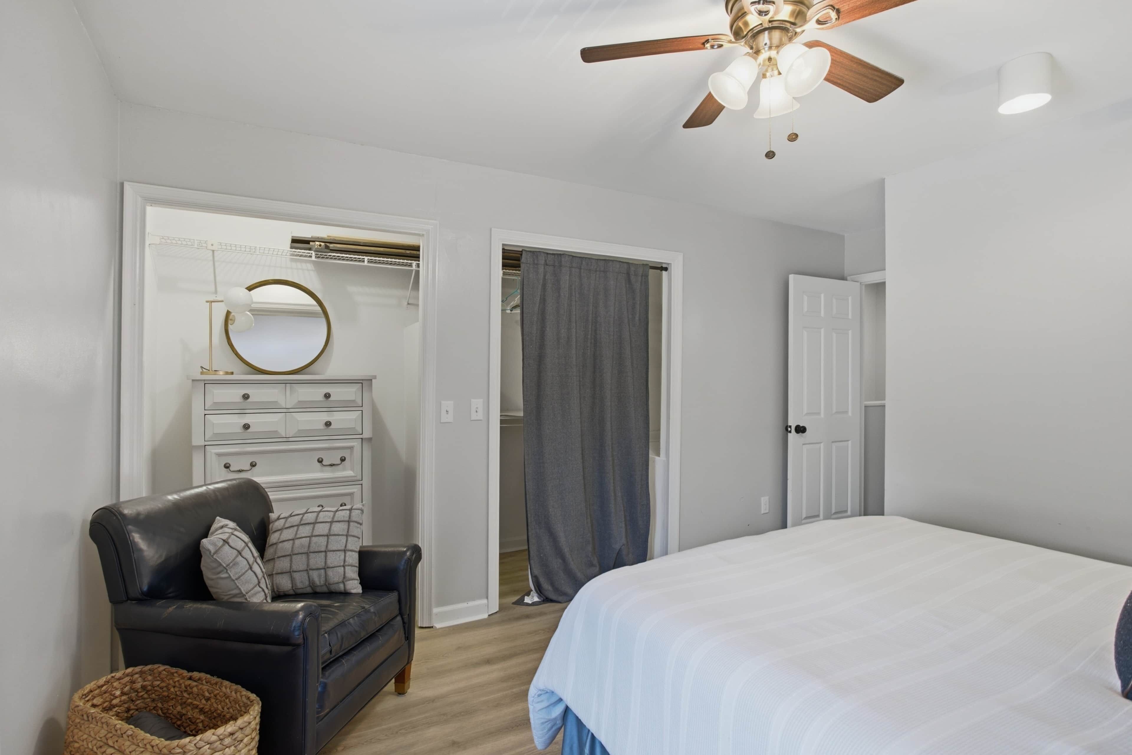 Ein Schlafzimmer mit Bett, Sessel, Kommode, Deckenventilator und Schrank.