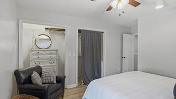 Ein Schlafzimmer mit Bett, Sessel, Kommode, Deckenventilator und Schrank.