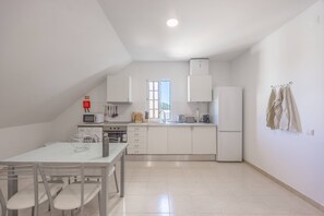Een moderne keuken met witte kasten, een eettafel met stoelen en een raam dat natuurlijk licht binnenlaat.