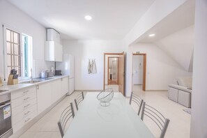 A modern kitchen with white cabinets, a dining table with chairs, and a view into the adjacent living area.
