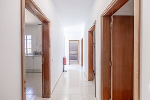 Corredor com portas de madeira, área de cozinha visível e um extintor de incêndio.