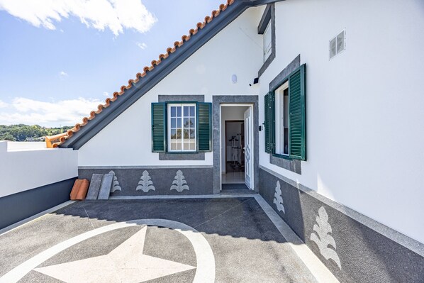 A building with a sloped roof, a door leading to an interior, and a decorative pattern on the ground.