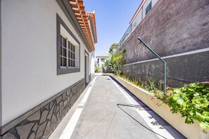 A narrow alleyway with a tiled floor, a stone wall on one side, and a building with a tiled roof and windows on the other. - Villa Palmeiras by YOUR KEY (Funchal)