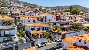 A residential area with multi-story houses, a street with parked cars, and a hillside in the background. - Villa Palmeiras by YOUR KEY (Funchal)