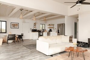 Amplia sala de estar con un sofá blanco, una mesa de comedor con sillas, una cocina con electrodomésticos modernos y un ventilador de techo.