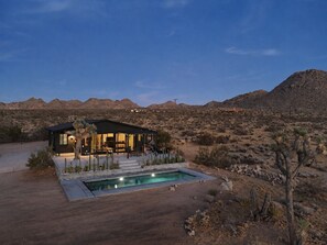 Una casa en el desierto con piscina, mobiliario exterior y vistas de las colinas circundantes.