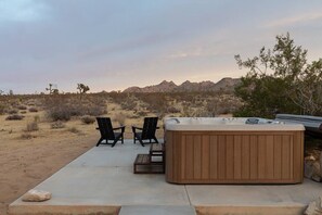Un jacuzzi con dos sillas, un patio de concreto y un paisaje desértico con montañas al fondo.