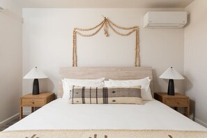 Una cama con cabecera de madera, dos mesitas de noche con lámparas y un aire acondicionado instalado en la pared.