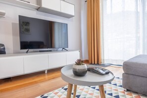 A modern living room with a flat-screen TV, a sofa, a small round table with a plant, and a remote control. - Vista Mar À Costa by YOUR KEY (Santa Cruz)