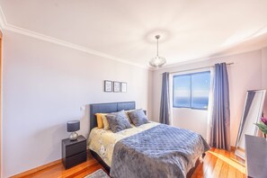 Une chambre à coucher avec un lit, une table de chevet, une lampe et une vue sur la mer par la fenêtre.
