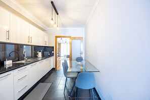Eine moderne Küche mit weißen Schränken, einer schwarzen Arbeitsplatte und einem Glastisch mit blauen Stühlen.