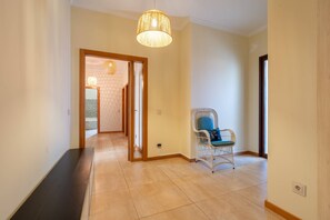 Un couloir avec un banc en bois, une chaise en osier dotée d’un coussin et un luminaire suspendu.