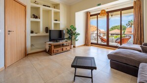 Una sala de estar con televisor, estanterías de madera, un sofá y vistas al exterior.