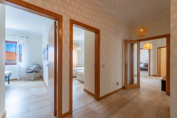Un hall d’entrée spacieux, avec des portes en bois donnant accès aux chambres, un coin repas avec une table et des chaises, et un salon avec un canapé et un luminaire suspendu.