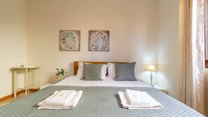 Habitación de hotel con cama, almohadas, mesita de noche, lámpara y dos obras de arte en la pared.