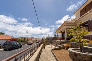 Une rue résidentielle avec un trottoir pavé, un mur en pierre et un petit arbre.