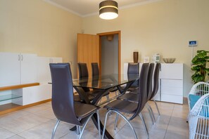 Un espace repas moderne avec une table en verre et des chaises en métal, un meuble blanc, une porte en bois et une petite plante.