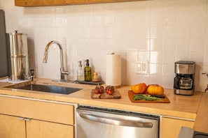 A modern kitchen with a stainless steel dishwasher, a coffee maker, and fresh produce on the counter. - Bed N` Burke | Pool + Spa | Peloton | Fire Pit (Yucca Valley)