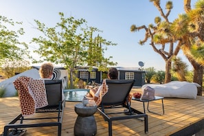 A deck with two lounge chairs, a small table with a bowl of fruit, and a water feature. - Bed N` Burke | Pool + Spa | Peloton | Fire Pit (Yucca Valley)
