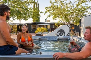 A hot tub with a unique design, surrounded by outdoor furniture and a building in the background. - Bed N` Burke | Pool + Spa | Peloton | Fire Pit (Yucca Valley)