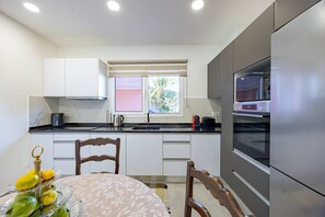 A compact kitchen with a built-in oven, a window with a view, and a dining area with a table set for two. - Vivenda Paz Lobo by Your Key (Santa Cruz)