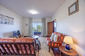A living room with a sofa, armchair, TV, and a table with a lamp. - Vivenda Paz Lobo by Your Key (Santa Cruz)