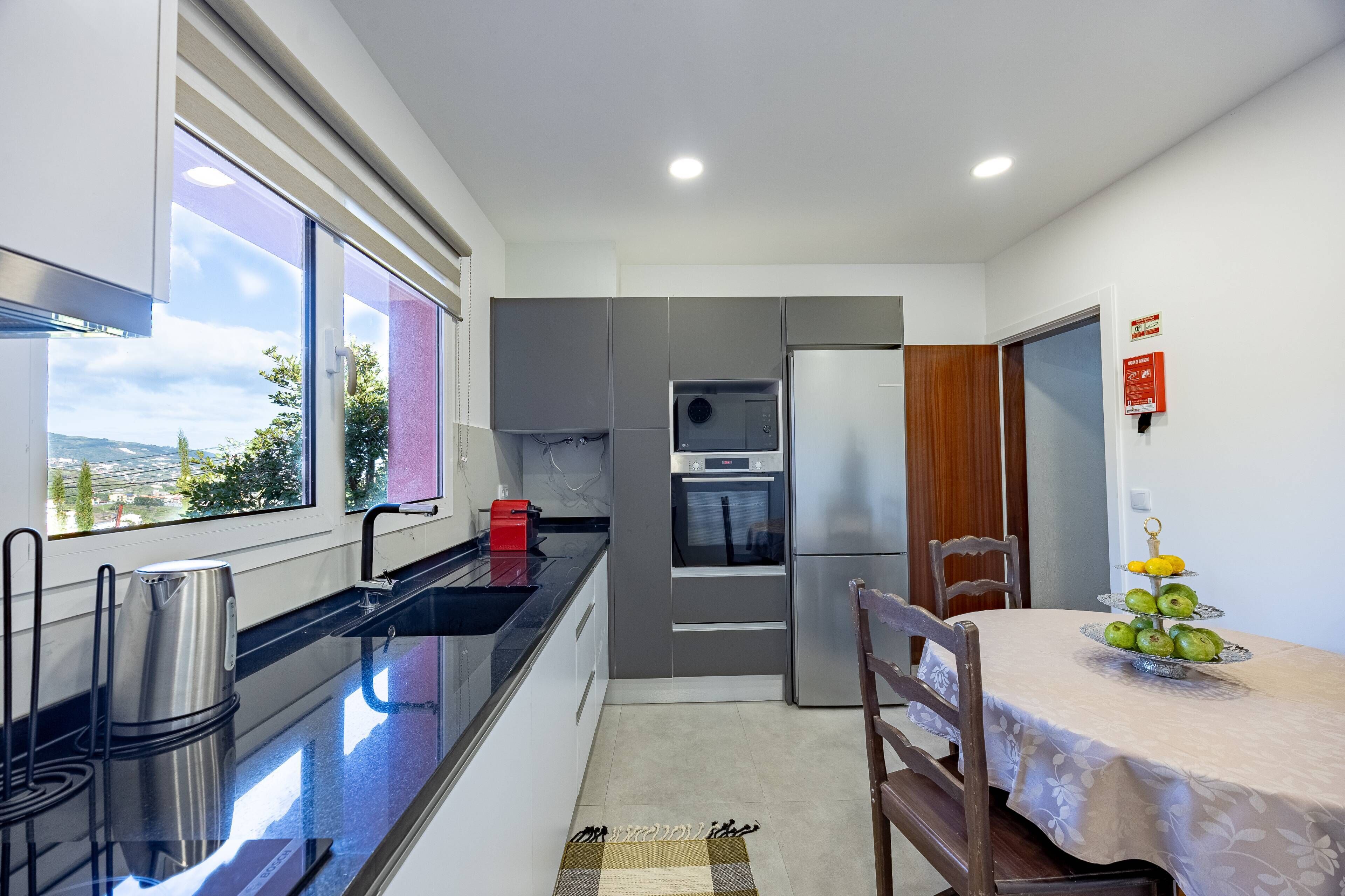 A modern kitchen with a built-in oven, a refrigerator, and a window with a view of the city.