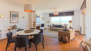 A spacious living area with a dining table, chairs, a sofa, and a view of the sea.