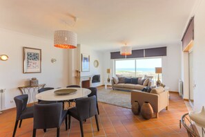 A spacious living area with a dining table, chairs, a sofa, and a view of the sea.