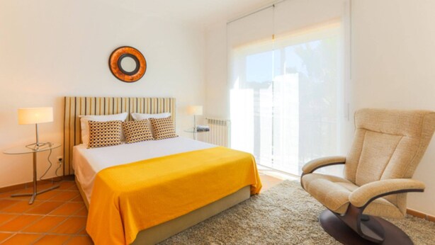 A bedroom with a bed, a chair, a lamp, and a window.