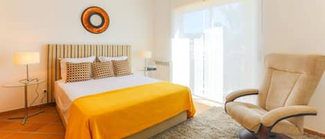 A bedroom with a bed, a chair, a lamp, and a window.