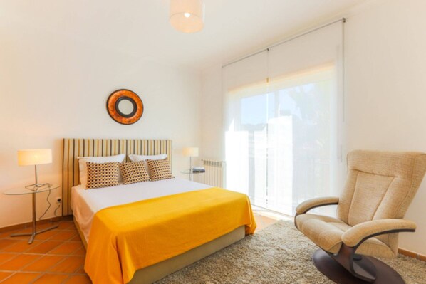 A bedroom with a bed, a chair, a lamp, and a window.