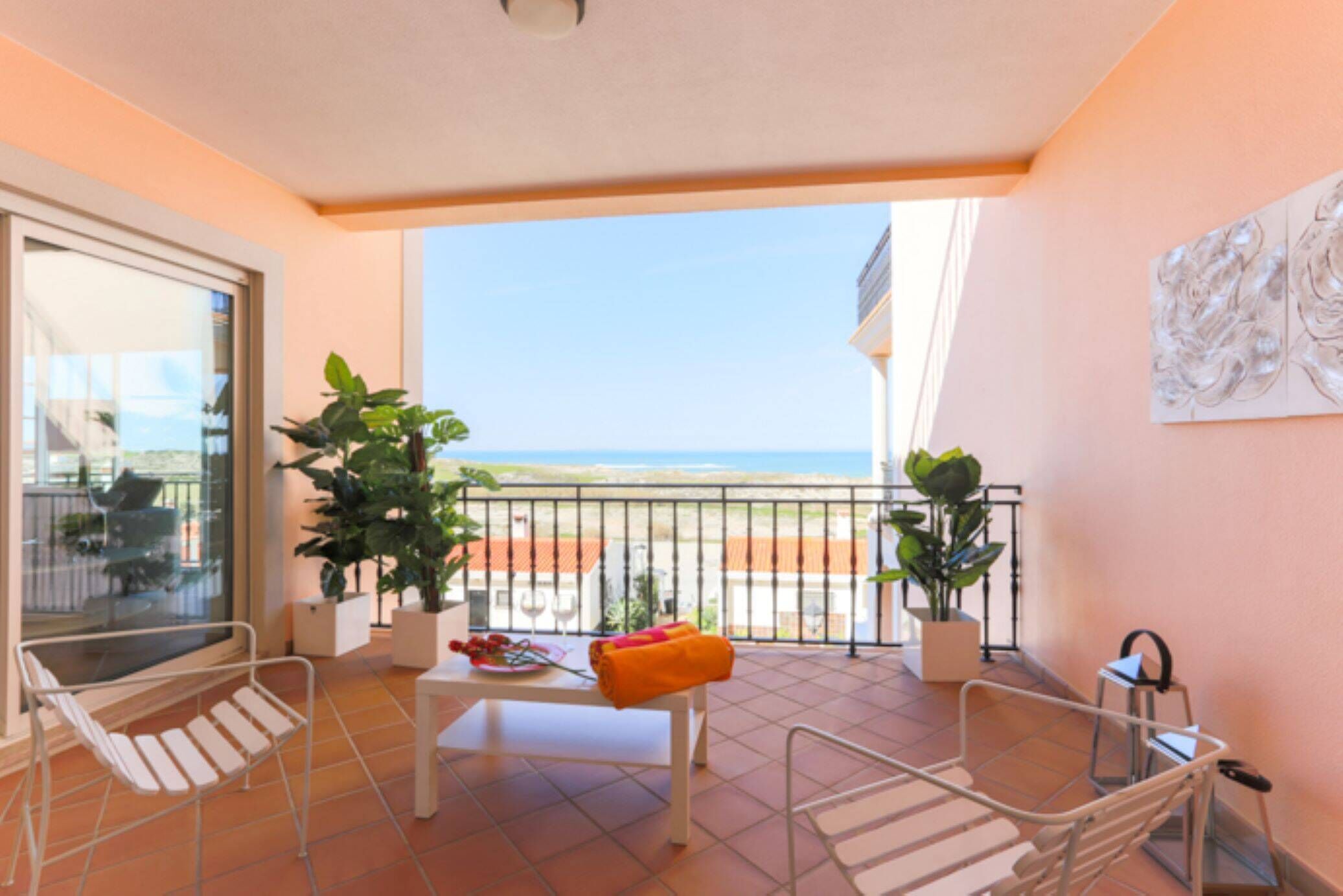 A balcony with a view of the sea, a table with chairs, and potted plants.