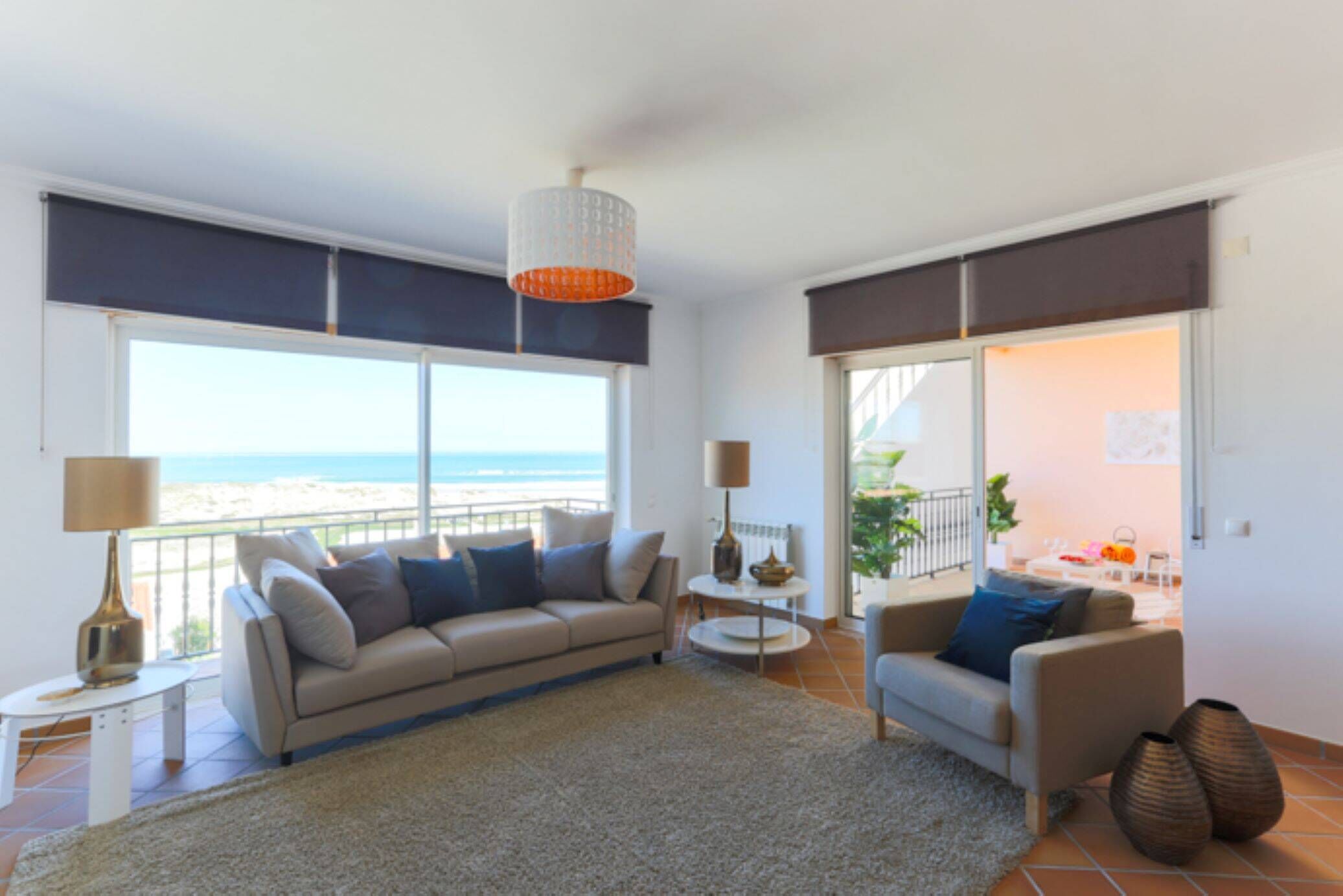 Un salon moderne avec un canapé, des fauteuils et une table basse. De grandes fenêtres offrent une vue sur la plage.