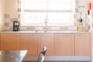 A kitchen with wooden cabinets, a stainless steel sink, and a window with a view of greenery. - Horizon Retreat, Sea View A12 (Óbidos)