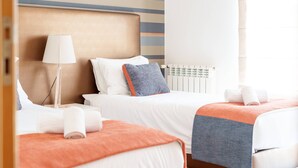 Et hotelværelse med to senge, en sengebordlampe, en radiator og et vindue med gardiner.